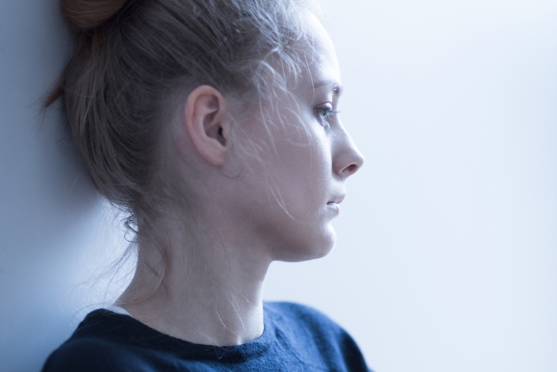 A sad woman leaning up against a wall.